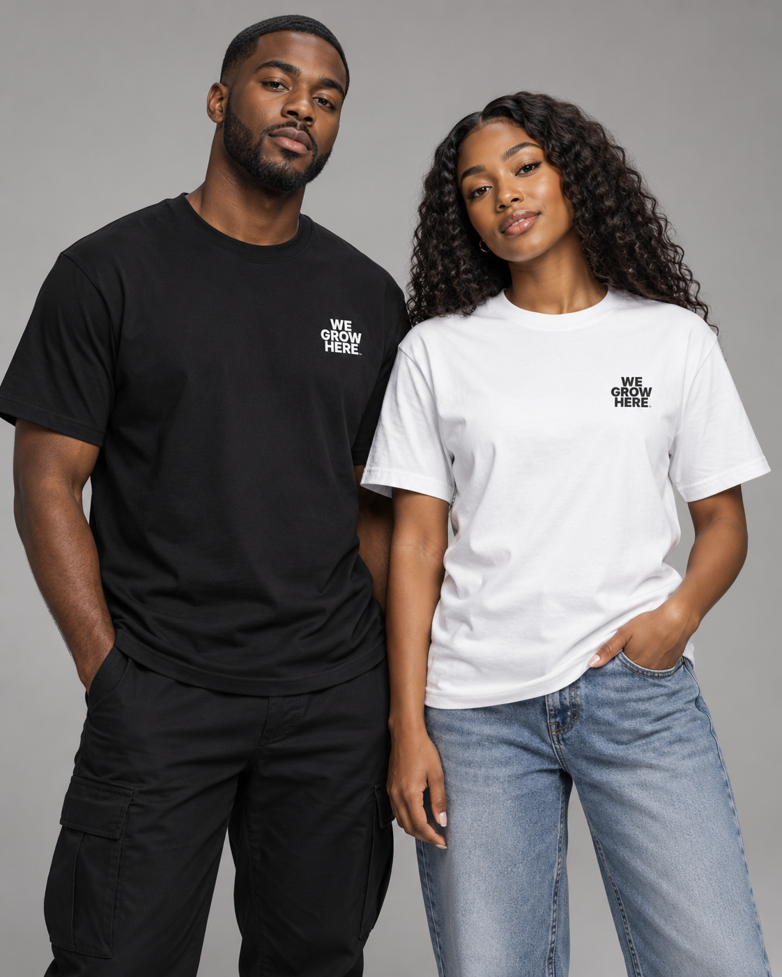 Two models wearing matching graphic t-shirts with the text 'WE GROW HERE.' printed on the left chest, one in black and one in white, posed against a solid gray studio background.